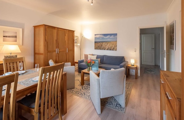 A modern living room with a dining area, wooden furniture, and a painting on the wall. - Haus Atrium Apartment 19 - Cozy 2-room vacation apartment with approx. 45 m², for (Sylt)