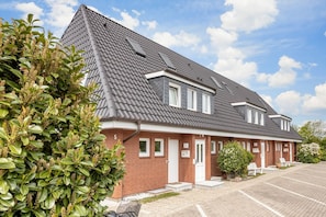 Un bâtiment en briques de deux étages, avec un toit recouvert de tuiles grises, un petit garage attenant et un espace de stationnement.