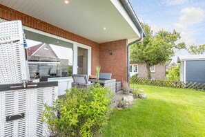 Une terrasse avec des meubles en osier, un mur en briques et une vue sur la maison.