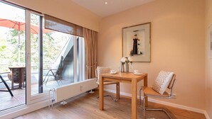 A modern room with a wooden table and chairs, a large window with curtains, and a framed picture on the wall. - Käpt`n Nelson, App 10 - Bright 2-room vacation apartment with approx. 52 m² living space, (Wenningstedt-Braderup (Sylt))