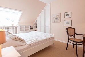 A bedroom with a bed, a chair, a desk, and a window.
