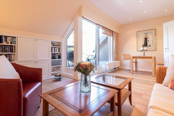 A spacious living room with a large window, a bookshelf, a coffee table, and a sofa.