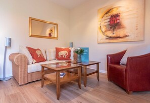 A living room with a sofa, a red armchair, a coffee table, a floor lamp, and a painting on the wall.