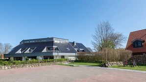 A modern building with a sloped roof, a stone wall, and a paved area with bicycles. - Käpt`n Nelson, App 10 - Bright 2-room vacation apartment with approx. 52 m² living space, (Wenningstedt-Braderup (Sylt))