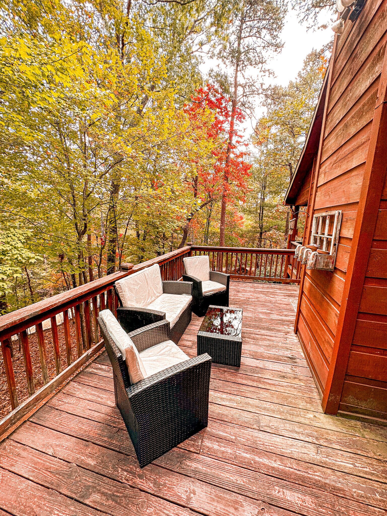 A wooden deck with wicker furniture and a view of autumn trees.