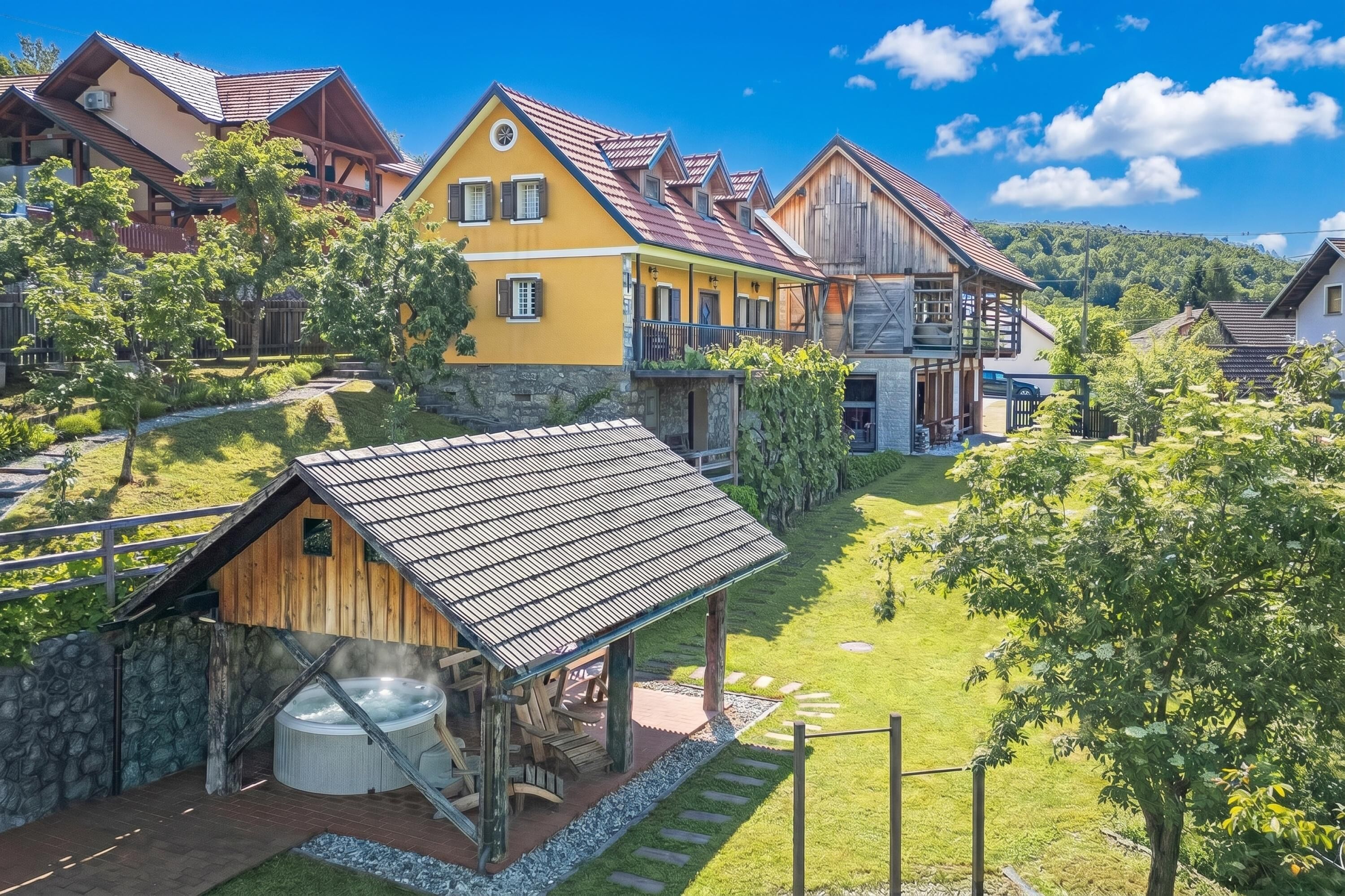 Ein traditionelles Holzhaus mit Whirlpool, umgeben von üppiger Vegetation und weiteren Holzbauten.