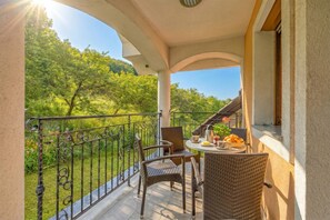 Ein Balkon mit Korbstühlen und einem Tisch, der auf eine üppige grüne Landschaft blickt.