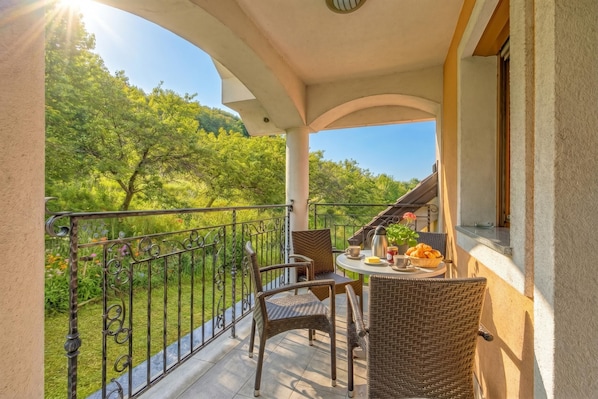 A balcony with wicker chairs, a table with breakfast items, and a view of greenery. - Pool Villa Silva Marija - App 206, Pišece, Slovenia (Pišece)