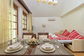 Un comedor con una mesa dispuesta para cuatro, un sofá cama con ropa de cama roja y blanca, y un aire acondicionado de pared.