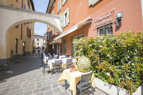 An outdoor café with tables and chairs, a large decorative bottle, and a hedge. - Kristall Lago Pool View, Desenzano Del Garda, Italy (Desenzano Del Garda)