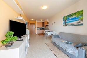 A modern living room with a flat-screen TV, a grey sofa, a dining area with a table and chairs, and a kitchen in the background. - Kristall Lago Pool View, Desenzano Del Garda, Italy (Desenzano Del Garda)