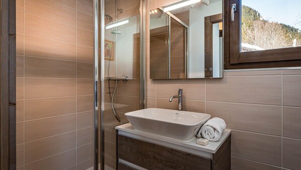 A modern bathroom with a glass shower enclosure, a white sink with a wooden vanity, and a large mirror above the sink.