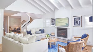 A spacious living room with a fireplace, a staircase, and a dining area. - This home matches quaint beachside charm with luxurious comfort. (Palm Beach)