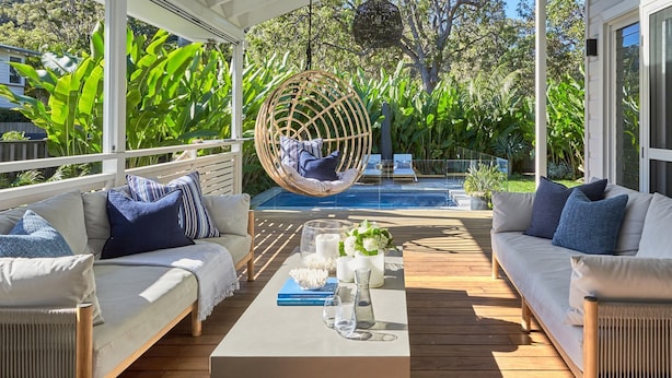 A sunlit outdoor seating area with a hanging chair, two sofas, and a table with drinks and flowers. - This home matches quaint beachside charm with luxurious comfort. (Palm Beach)