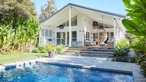 A modern house with a pool, outdoor seating, and lush greenery. - This home matches quaint beachside charm with luxurious comfort. (Palm Beach)