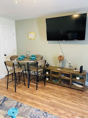 Un coin repas avec une table et des chaises, un téléviseur fixé au mur et un meuble en bois avec des étagères.