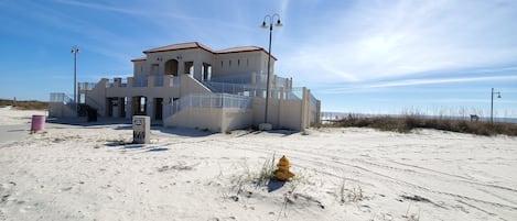 Ein Gebäude direkt am Strand mit einer Treppe zum Eingang, einem gelben Feuerlöscher und blauem Himmel.