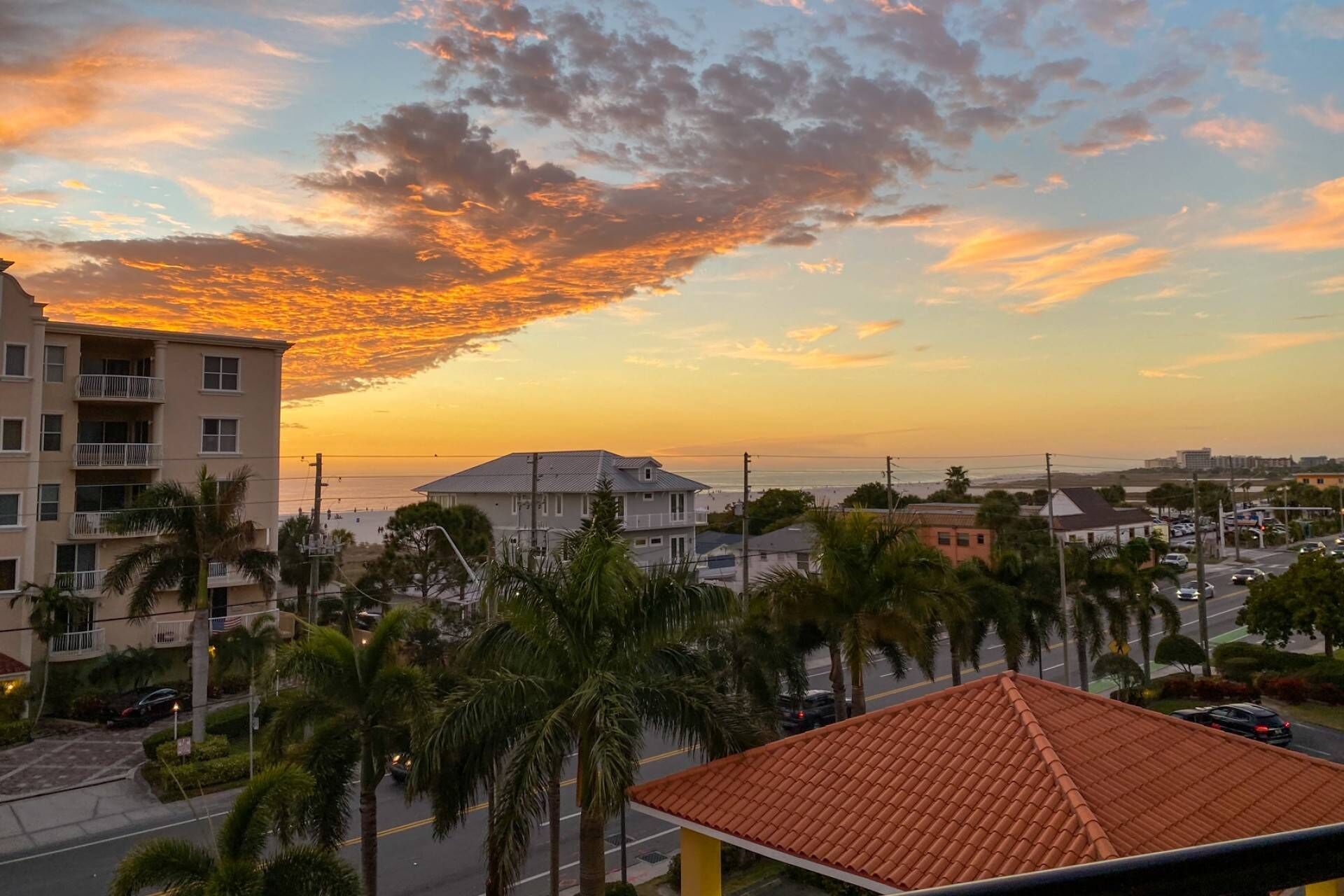 Un quartier résidentiel en bord de mer offrant une vue sur le coucher du soleil, avec des immeubles à plusieurs étages, des palmiers et un ciel dégagé.