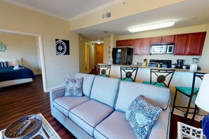 Kodikas olohuone, jossa on sohva ja nojatuoleja, keittiö puukuvioisilla kaapeilla ja kodinkoneilla sekä käytävä, joka johtaa toiseen huoneeseen.
