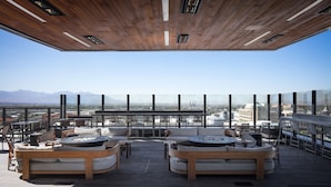Une terrasse sur le toit, aménagée avec des meubles en bois, un foyer et offrant une vue sur la ville.
