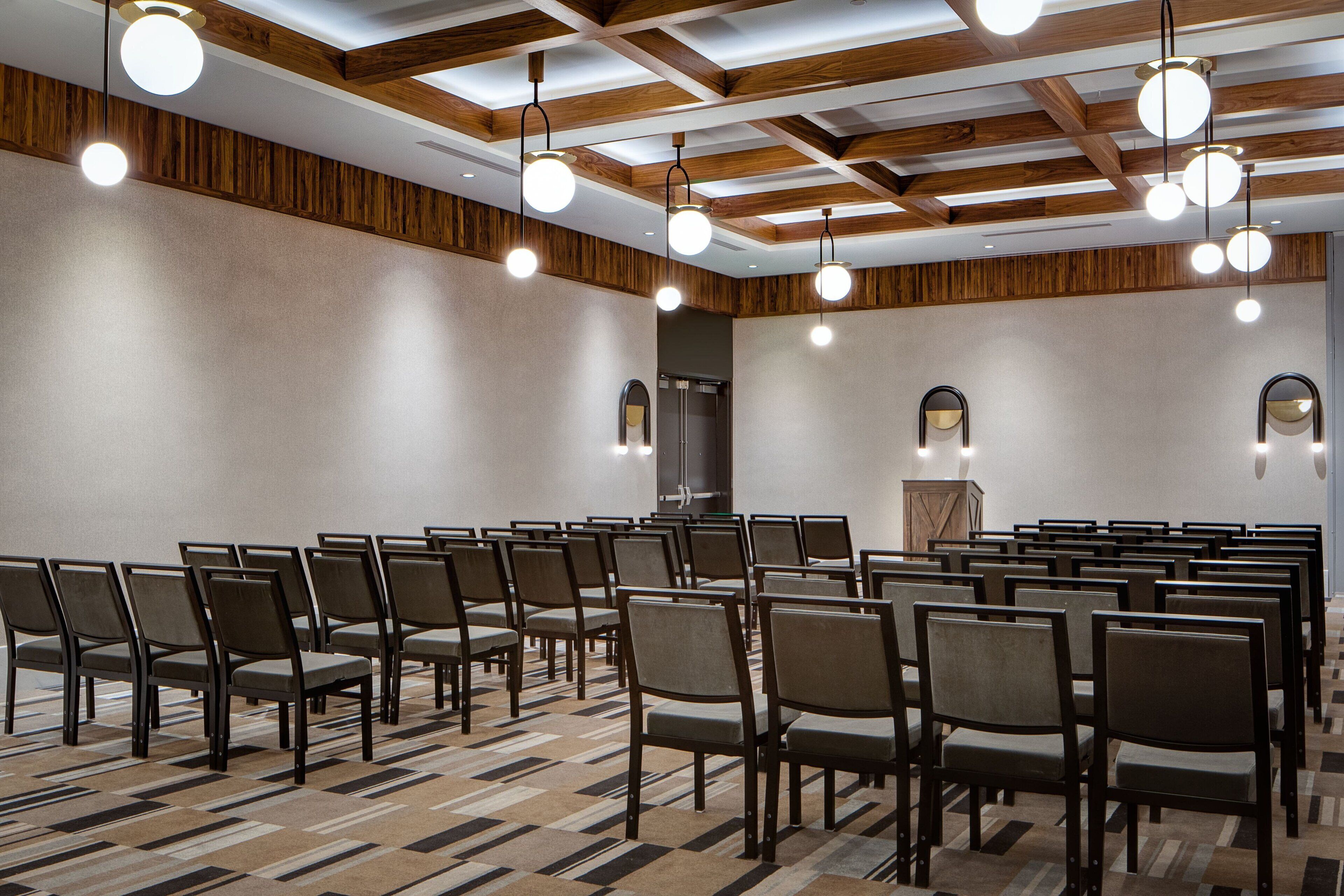 A conference room with rows of chairs, a podium, and ceiling lights.