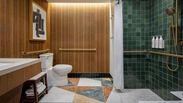 A modern bathroom with a wooden vanity, a toilet, a shower with a gold showerhead, and a tiled floor.