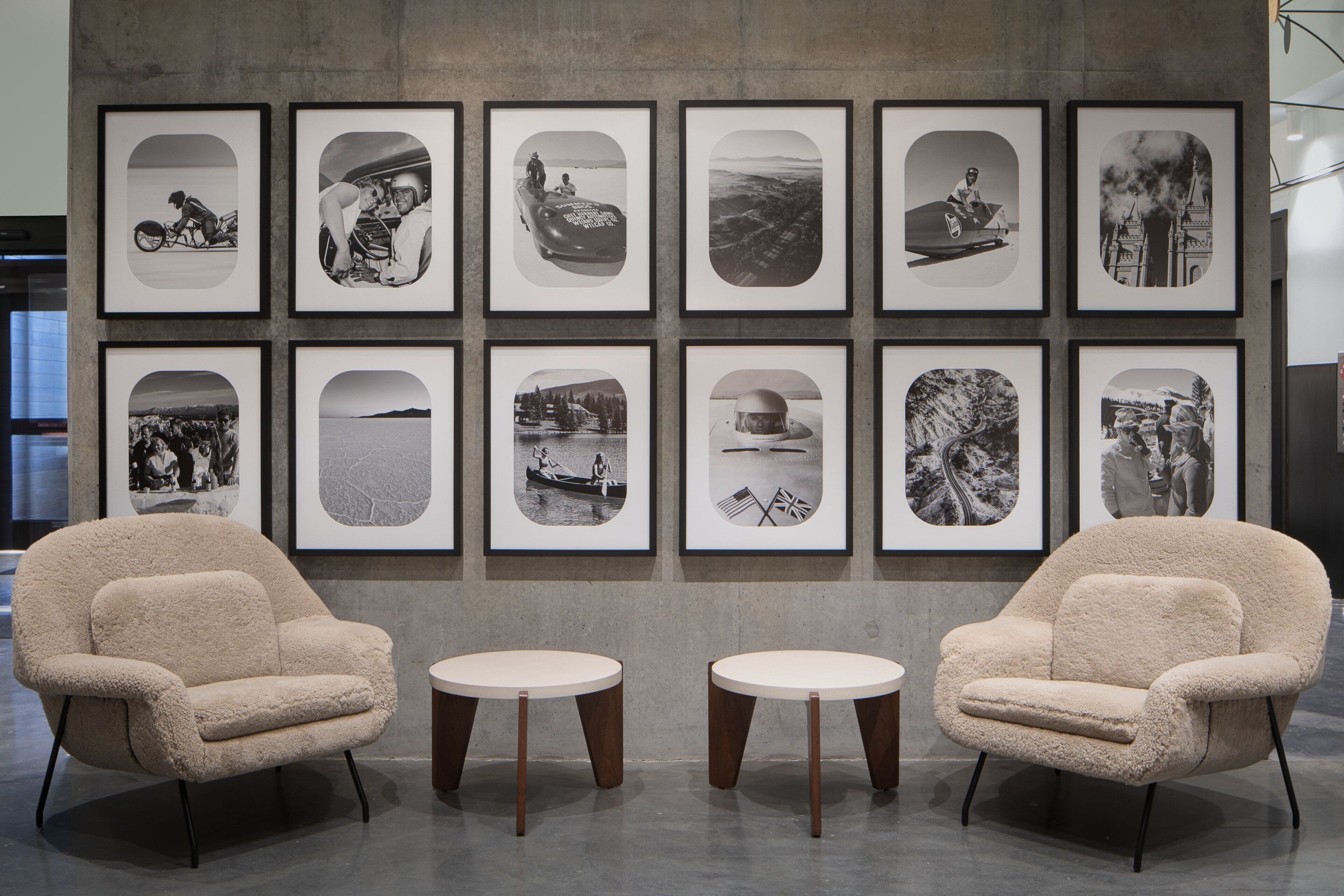Un interno moderno con due poltrone confortevoli e piccoli tavolini rotondi, fotografie in bianco e nero appese al muro e un pavimento in cemento.