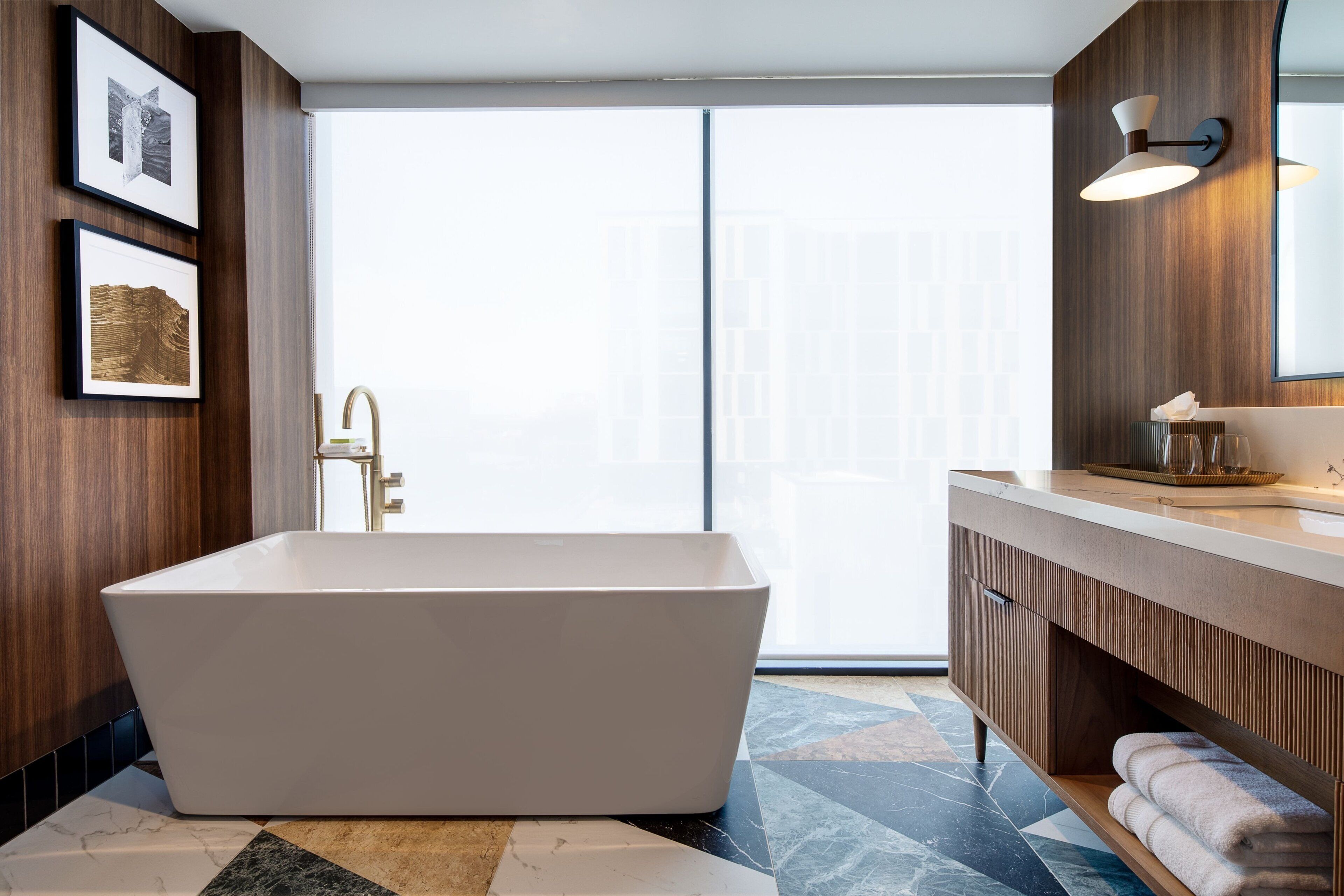 A modern bathroom with a freestanding bathtub, wooden paneling, a large mirror, and a tiled floor.