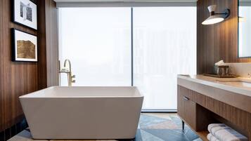 A modern bathroom with a freestanding bathtub, wooden paneling, a large mirror, and a tiled floor.