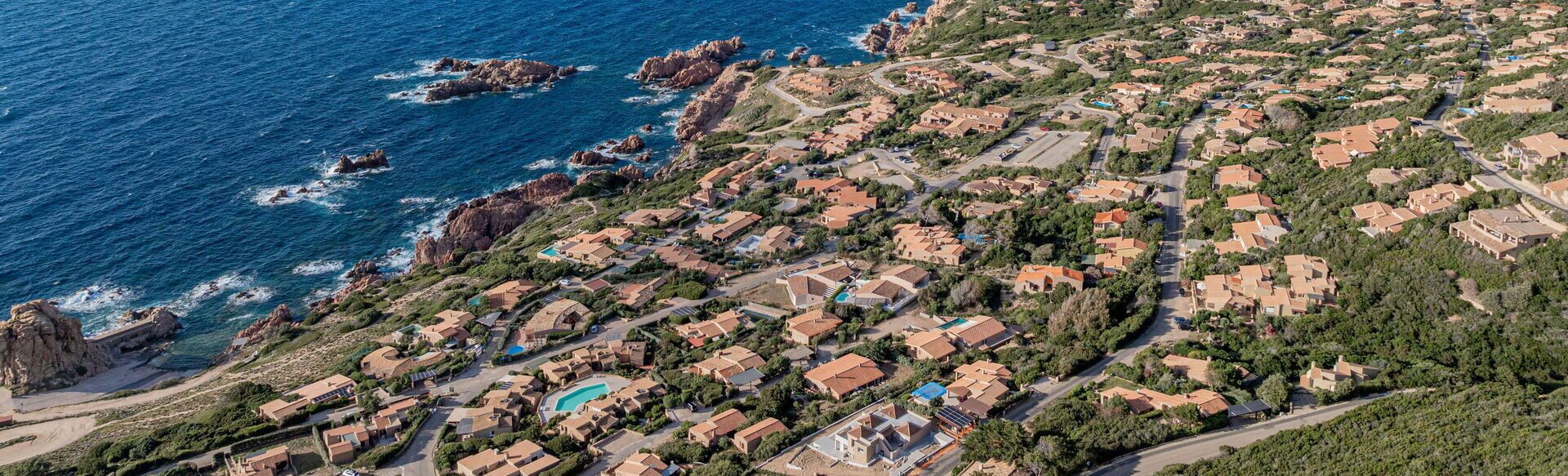 Oversigtsbillede af et kystnært boligområde med huse, veje og en strand.