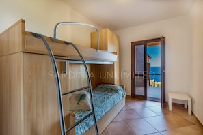 Una habitación con una cama litera, una escalera, un banco y una puerta que da a un balcón con vistas al mar.