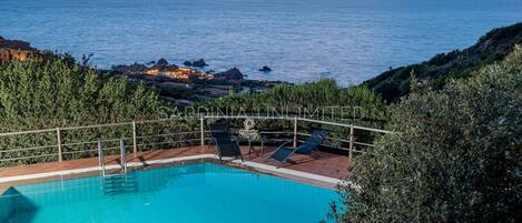 A swimming pool with a view of the sea and rocky coastline.