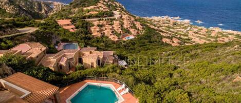 A coastal villa with a swimming pool, terraced houses, and a view of the sea.