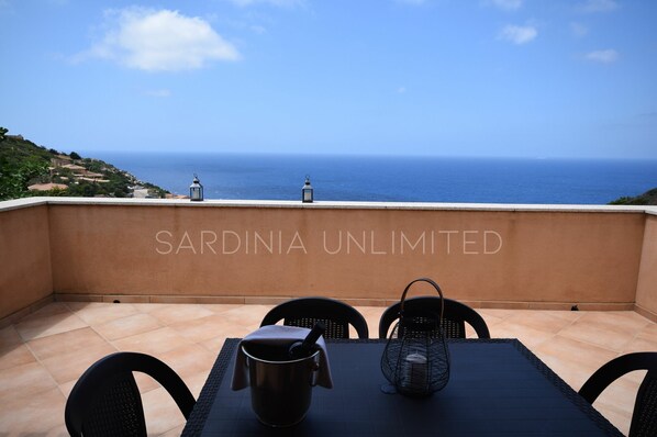Une terrasse avec vue sur la mer, une table avec des chaises et deux lanternes.