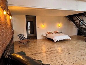 Experience the industrial-chic ambiance in this stylish room, featuring a large bed, wooden staircase, and exposed brick walls.
