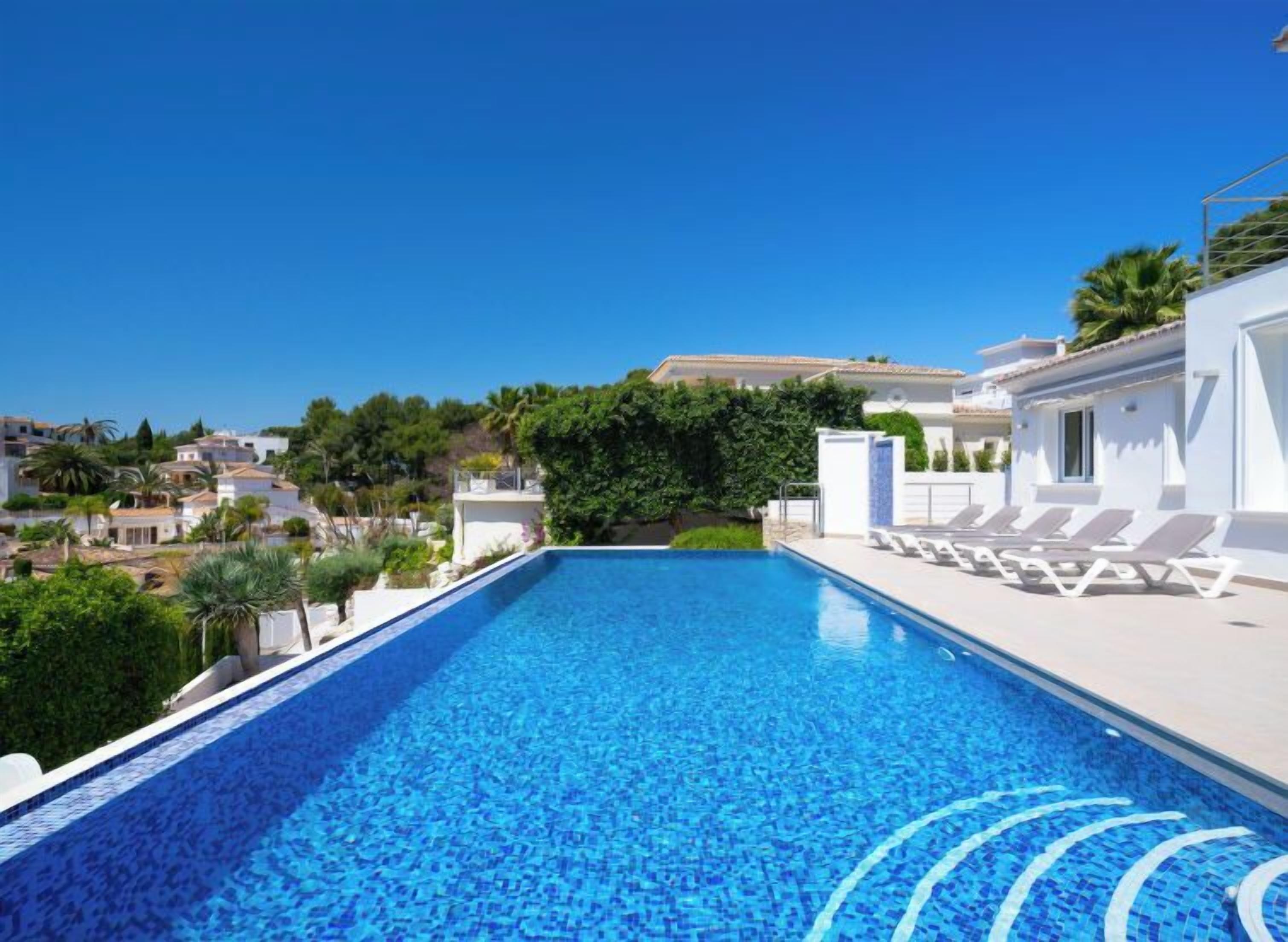 A swimming pool with clear blue water, surrounded by white buildings and greenery.