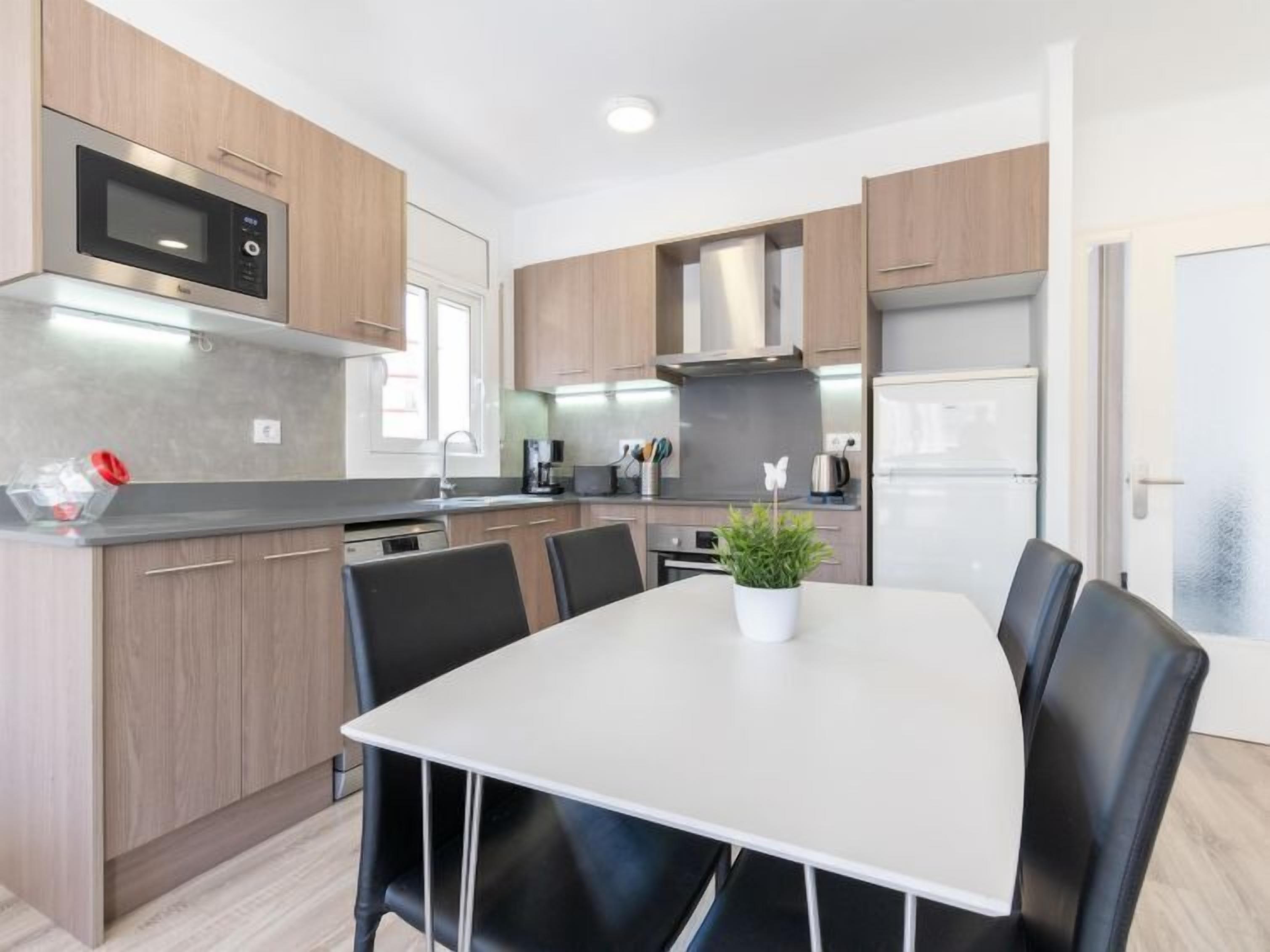 A modern kitchen with wooden cabinets, a stainless steel microwave, a refrigerator, and a dining table with chairs.