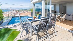 Un área de comedor al aire libre moderna con piscina, con vistas a una ciudad costera.