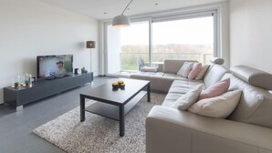 A modern living room with a sofa, a coffee table, a TV, and a balcony with a view. - Solis with balcony by Interhome (Bredene)