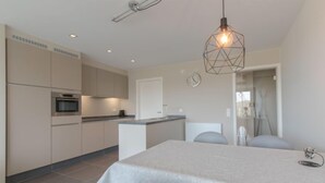 A modern kitchen with a dining area, featuring a large island, built-in appliances, and a geometric pendant light. - Solis with balcony by Interhome (Bredene)