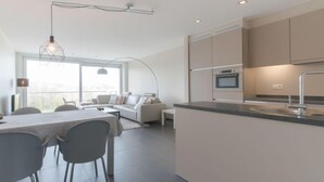 A modern kitchen with a central island, built-in appliances, and a dining area with a table and chairs. - Solis with balcony by Interhome (Bredene)