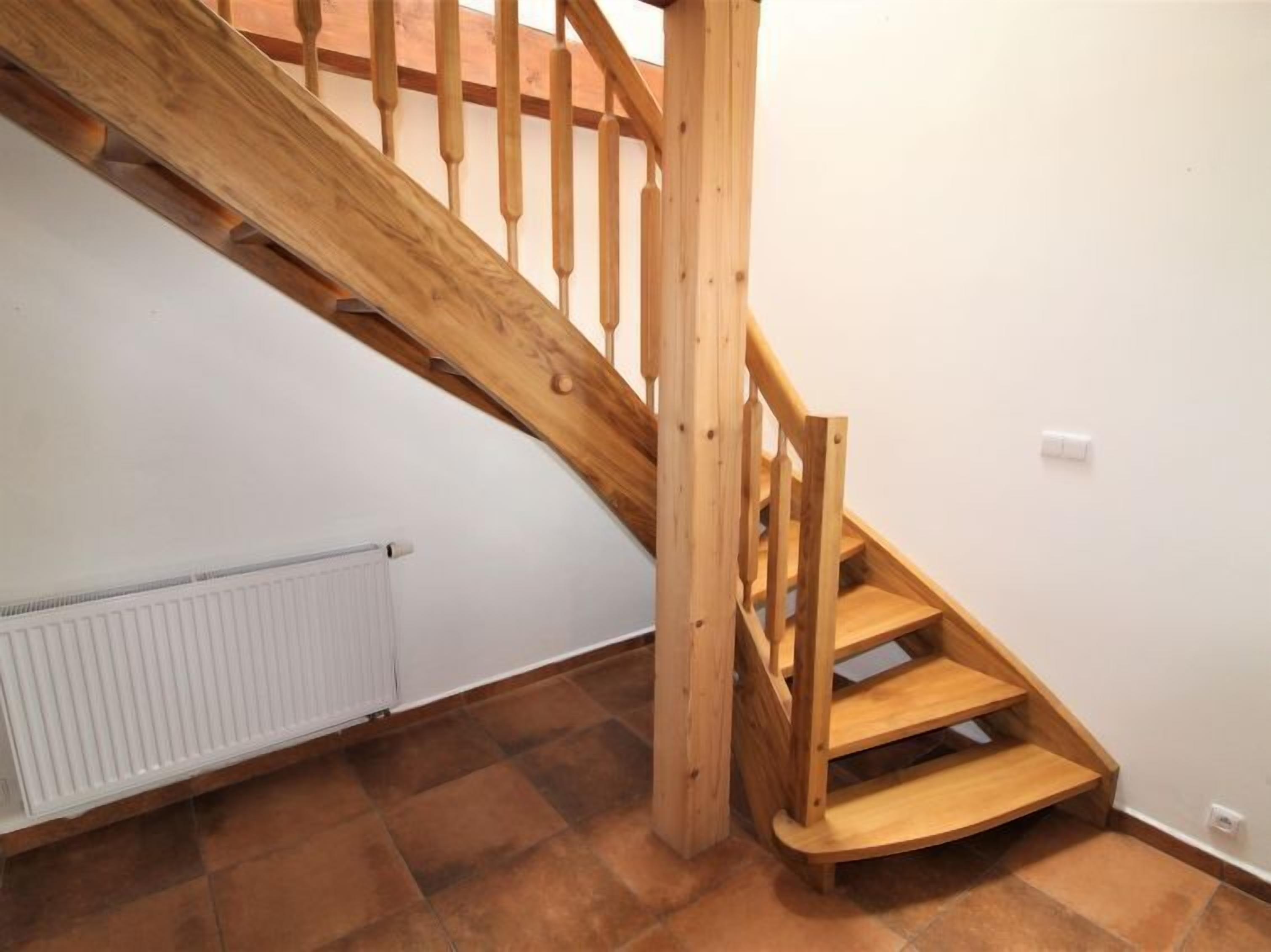 Un escalier en bois, avec un radiateur blanc et un sol carrelé de couleur marron.