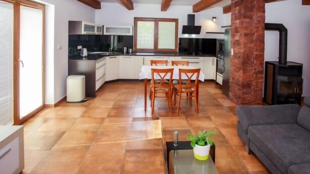 Una cocina moderna con armarios blancos, una zona de comedor con mesa y sillas, un sofá gris y una chimenea de ladrillo.