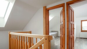 Una habitación con techo inclinado, suelo de madera y una escalera de madera con barandilla.