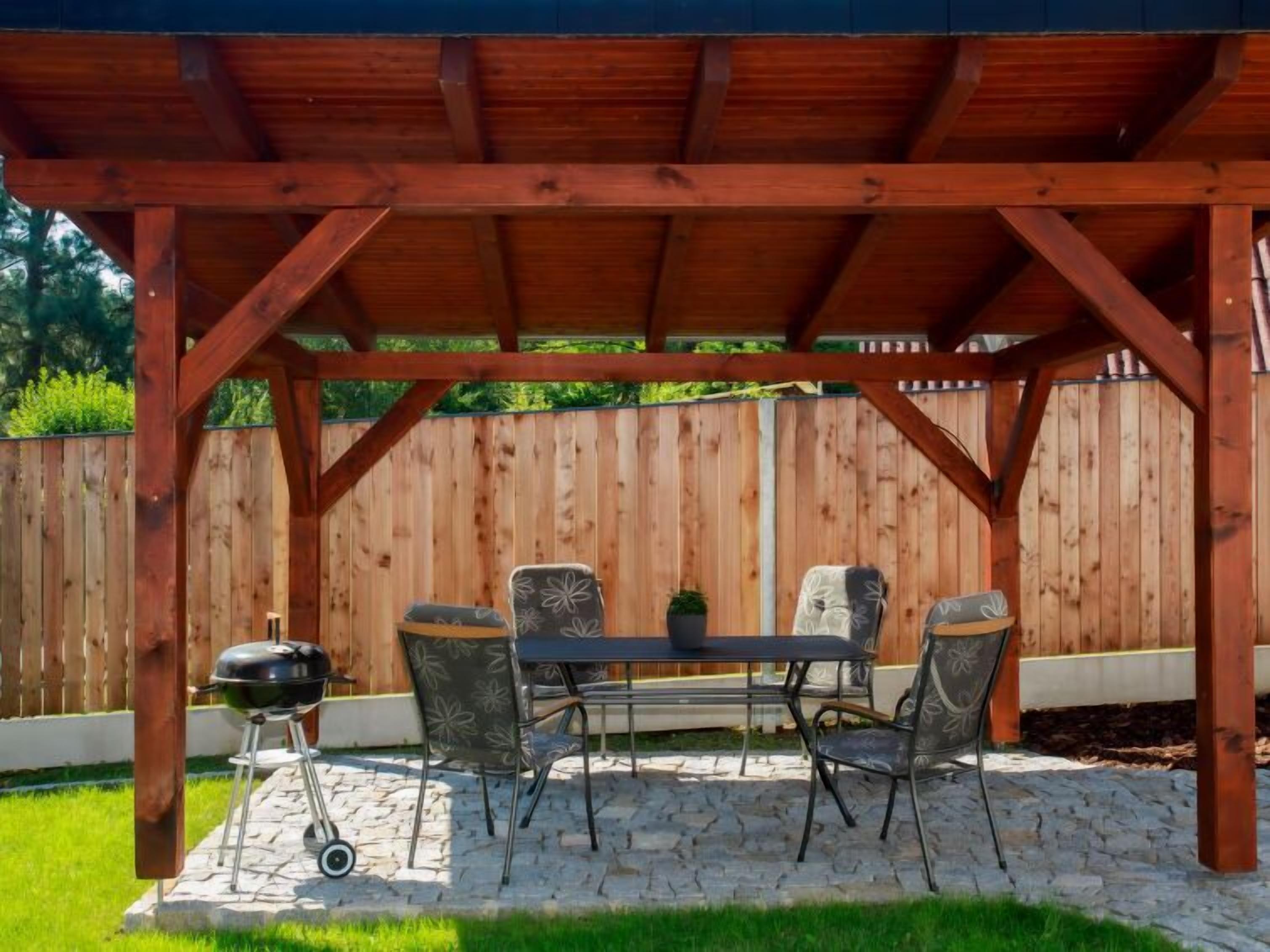 A covered patio with a stone floor, a table, four chairs, and a barbecue grill.