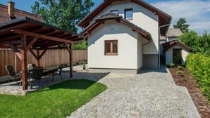 Una casa con un camino de piedra que lleva a una terraza de madera, patio trasero cercado y un pequeño jardín.