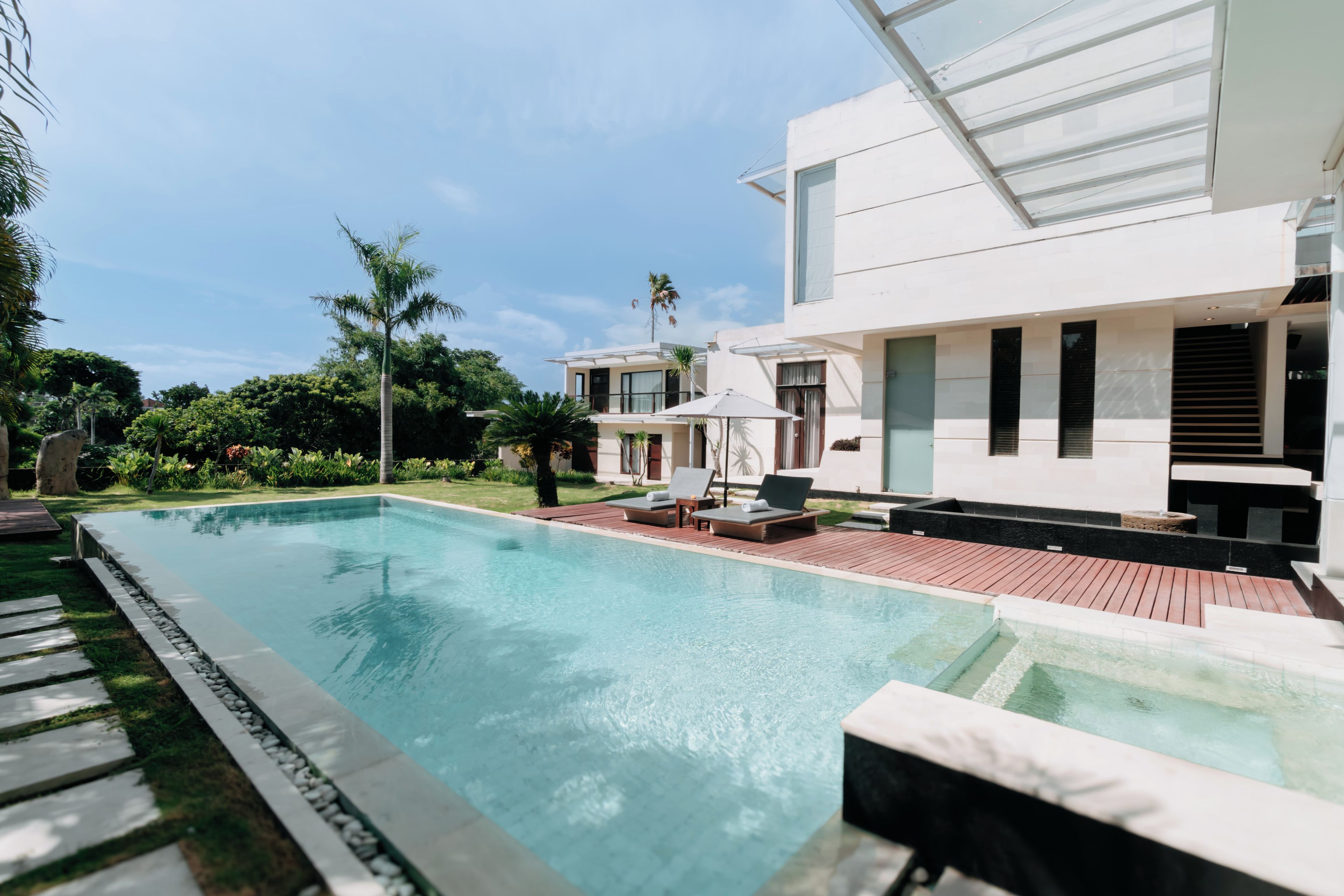 A modern pool area with a clear pool, lounge chairs, and a wooden deck.