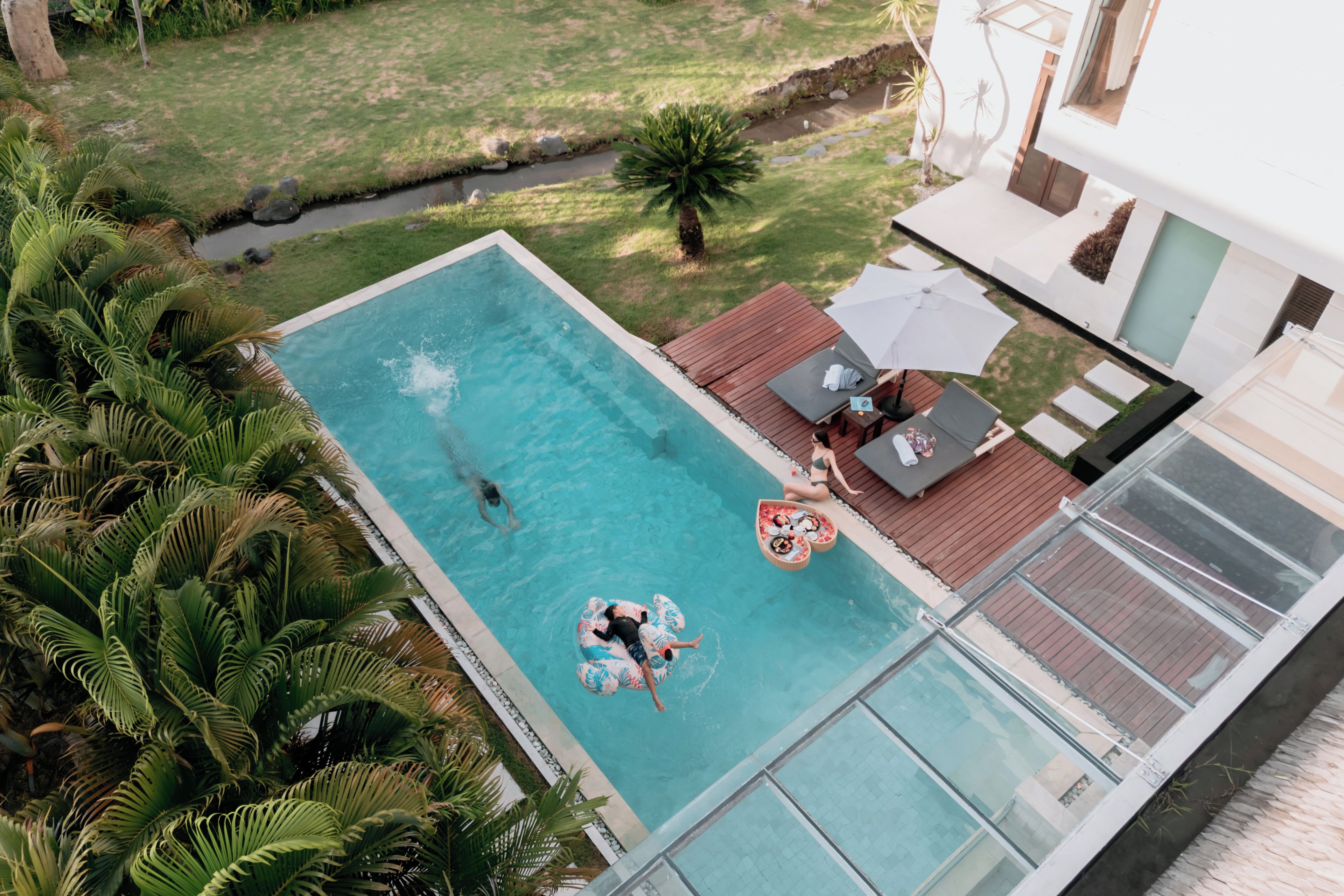 An aerial view of a swimming pool with a wooden deck, lounge chairs, and a small boat.