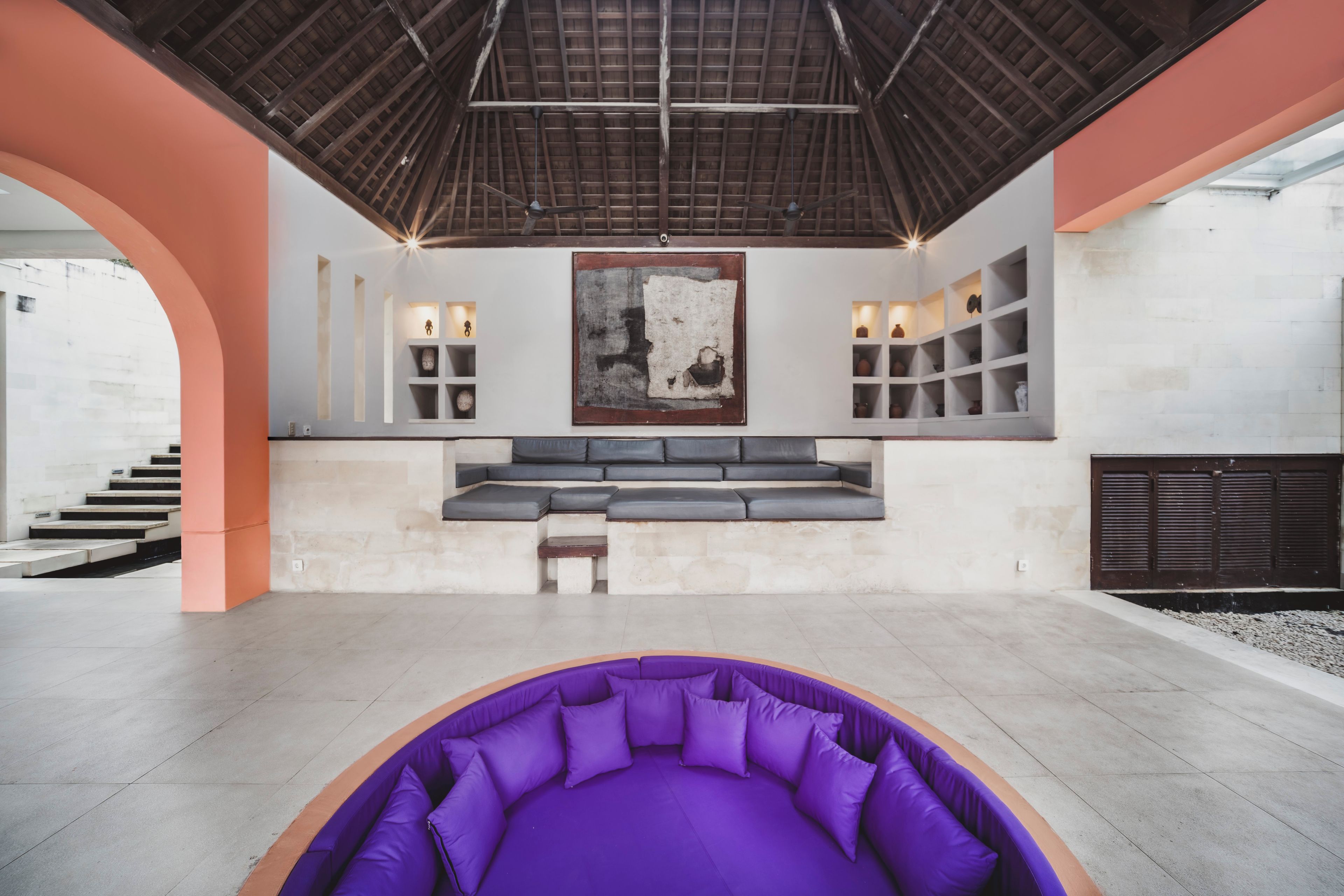 Un interior moderno con una zona de estar morada, una escalera y un cuadro abstracto grande.