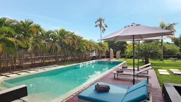 Et rektangulært swimmingpool med en træterrasse, liggestole og en pergola med parasol.